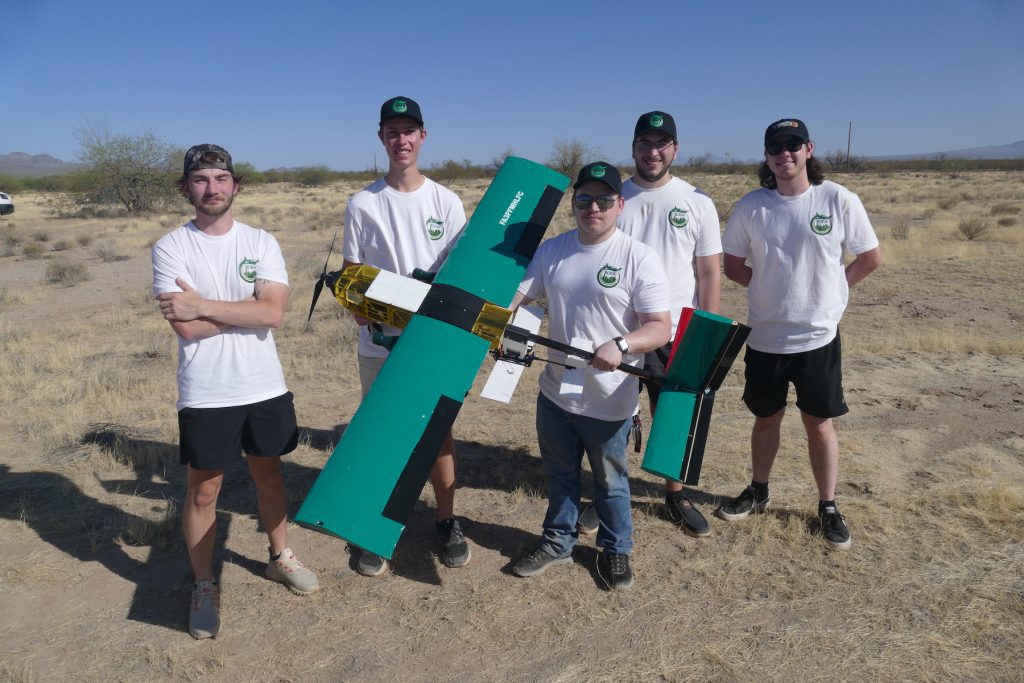 UNC Charlotte AIAA team members stand in field with airplane