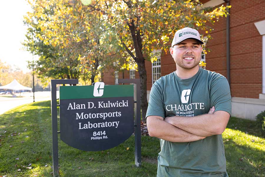 Layne Riggs standing beside sign for Alan D. Kulwicki Motorsports Laboratory