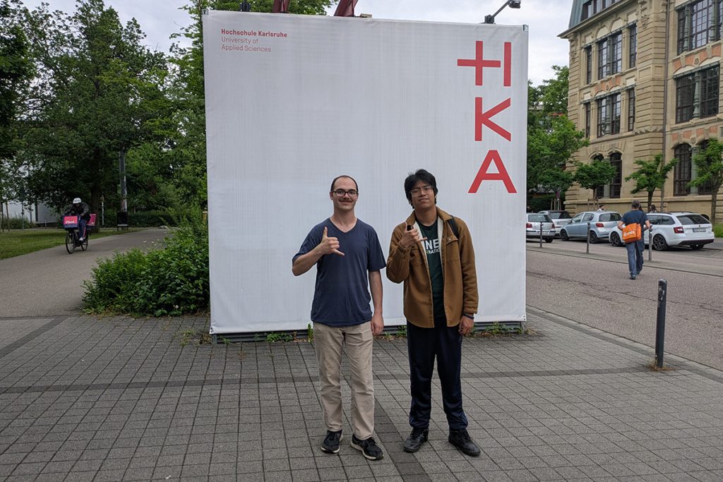 Two Niner Engineering students standing in front of a sign for HKA in Germany