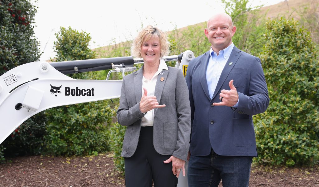 Two people standing near Bobcat machinery