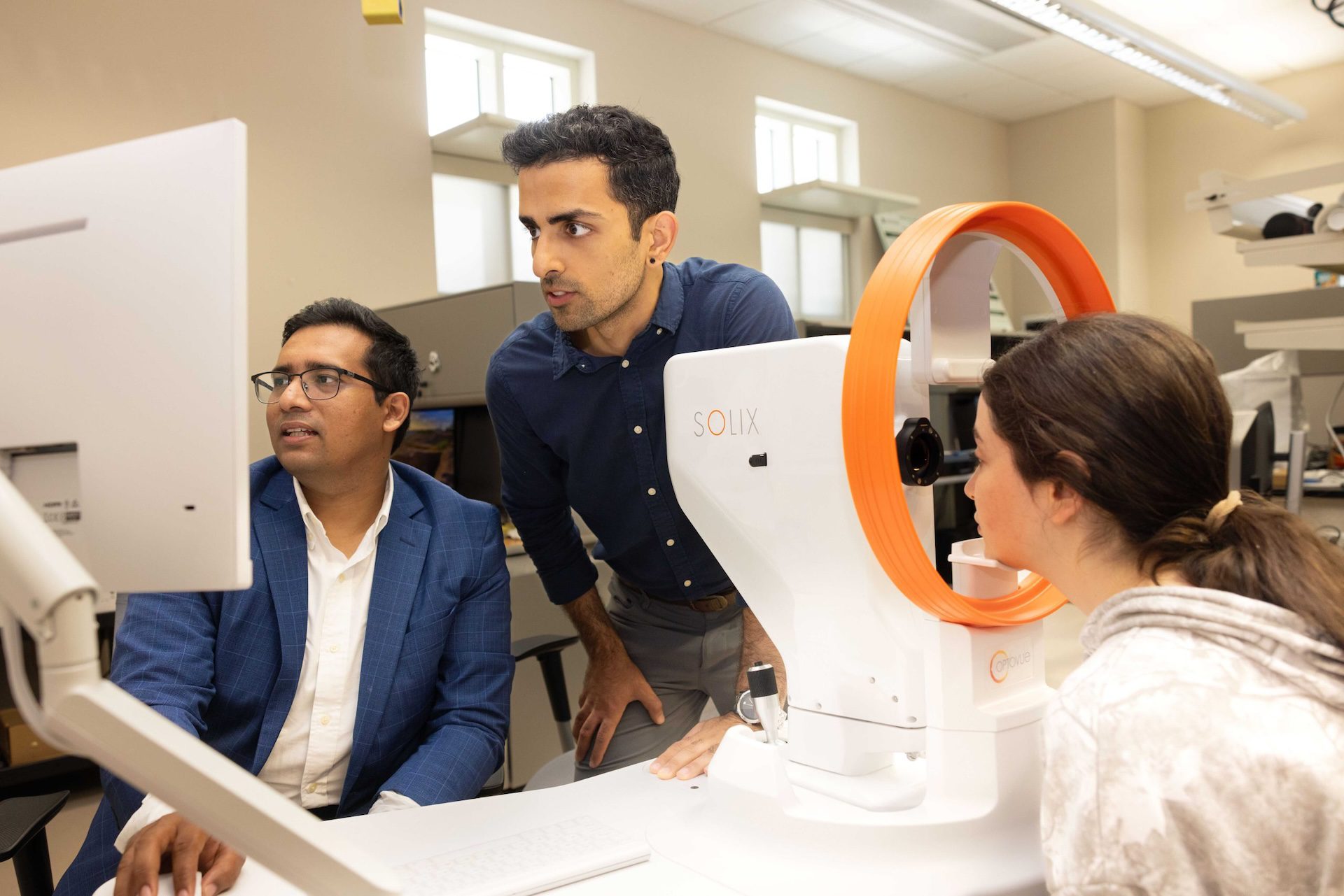 Minhaj Nur Alam and Sina Gholami look at computer while another individual looks into Solix machine