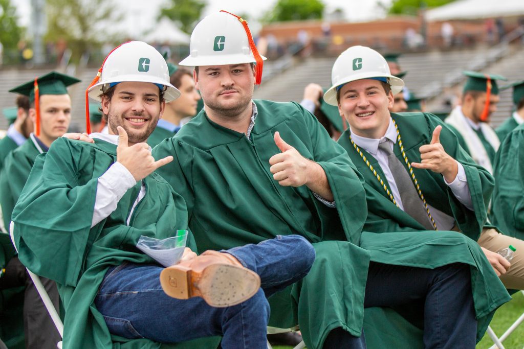 Construction Management graduates in their graduation robes and hats showing pick axe hand signs