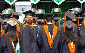 Male student dressed in regalia smiles at the camera during commencement