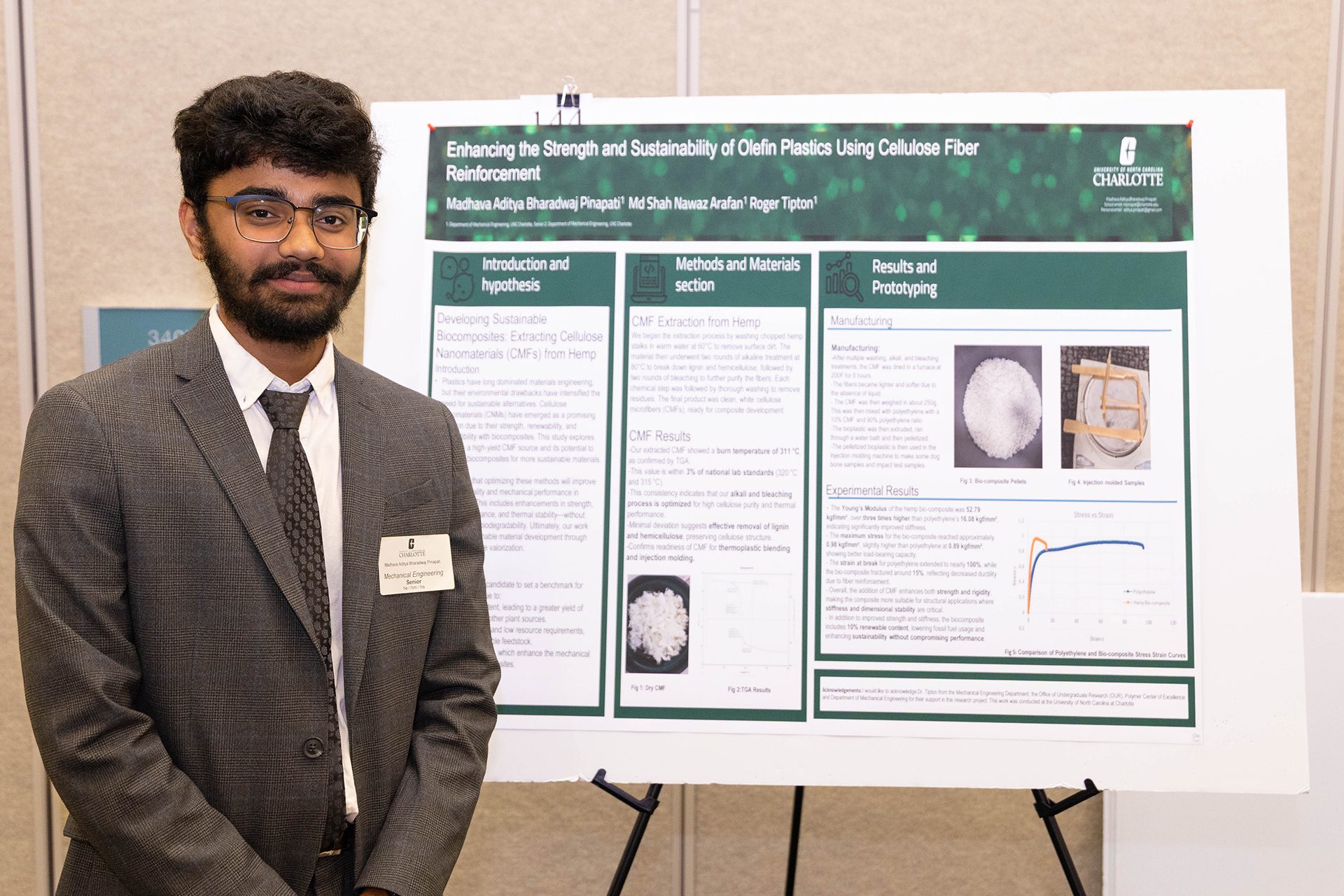 Male engineering student stands smiling in front of presentation poster.
