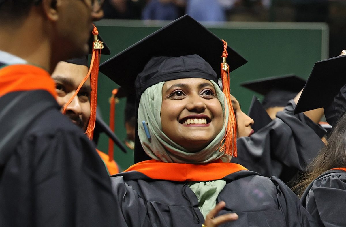 Female graduate student dressed in regalia looking up and smiling at Commencement