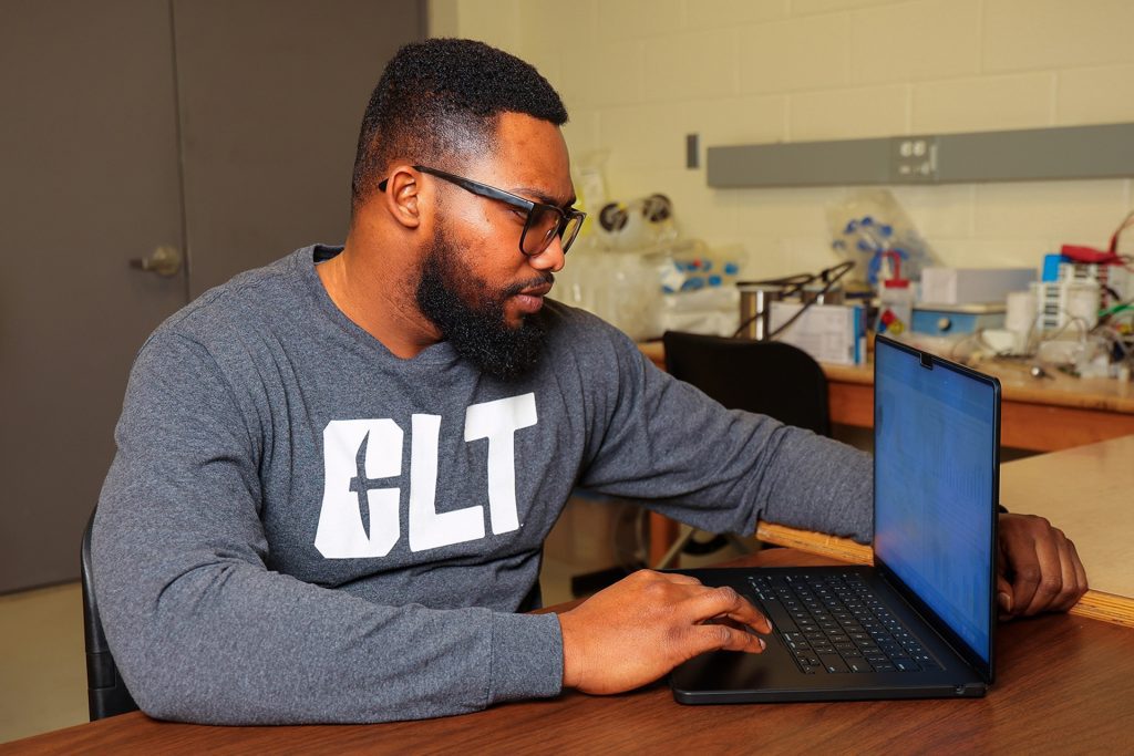 Felix Ekuful, sitting at a table, and works on a laptop.