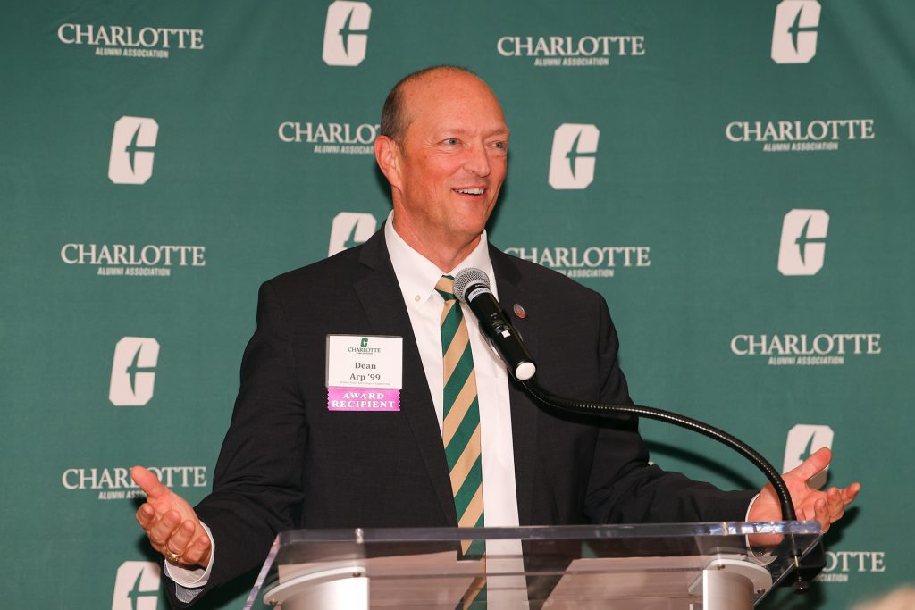 Dean Arp speaks from a podium in front of a green Charlotte backdrop