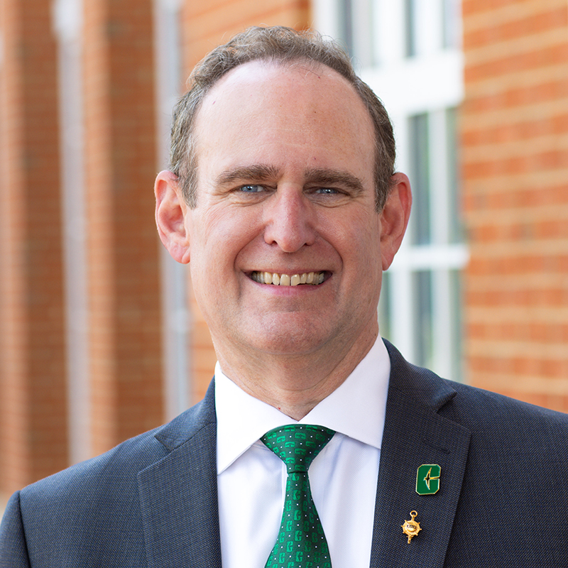 Portrait of Rob Keynton wearing a coat and tie and standing outside near a brick building